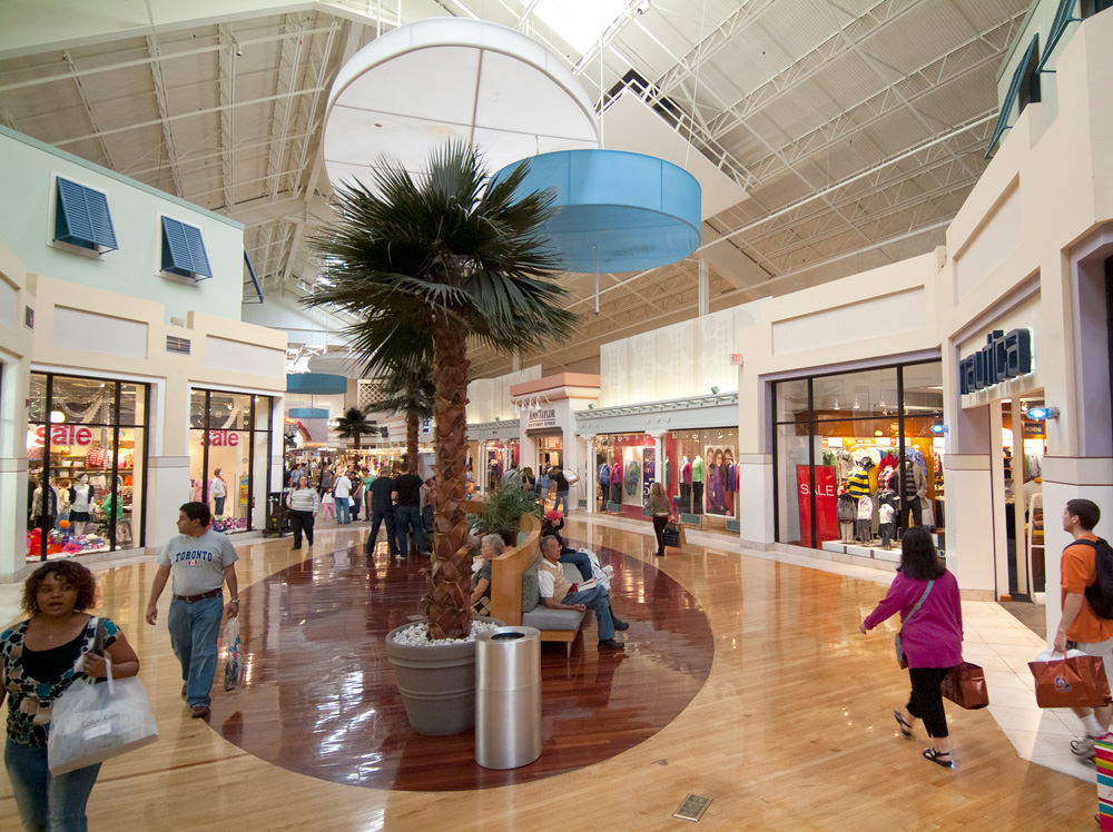 Interior de un outlet en Sawgrass Mills con tiendas de ropa de marca y pasillos llenos de compradores.