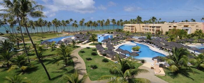 Un resort en Brasil rodeado de palmeras, piscinas y acceso directo a una playa de aguas turquesa. Vista aérea de resort all inclusive en Brasil con piscina, jardines tropicales y playa al fondo.