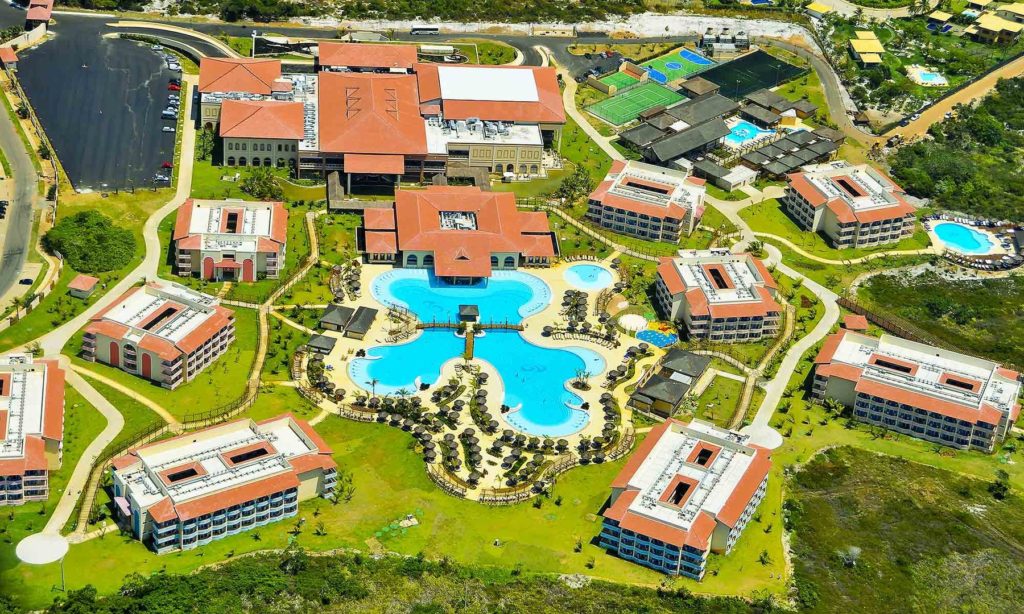 Resort all inclusive en Brasil con piscina gigante y alojamiento de lujo Vista aérea de un resort all inclusive en Brasil con gran piscina central y edificios rodeados de jardines.