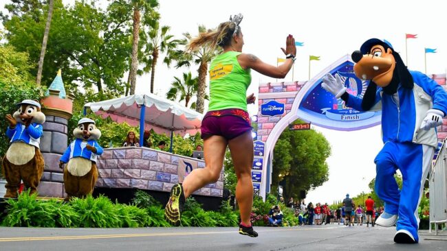 Una corredora celebra con Goofy en la meta de runDisney, un clásico evento deportivo en Walt Disney World.