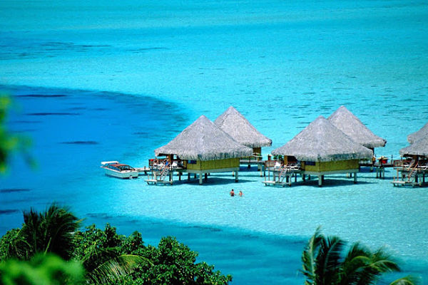 Bungalows sobre el agua en playa de aguas cristalinas color turquesa en destino paradisíaco tropical