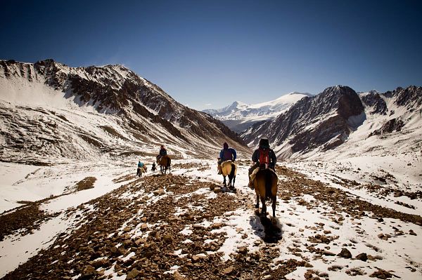 grupo de personas cabalgando en los andes sobre las montañas nevadas