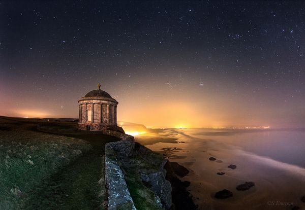 Costa de Irlanda de noche con templo de Mussenden, acantilados y cielo estrellado sobre el océano