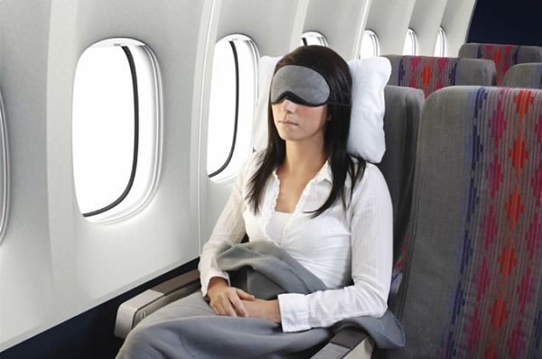 Mujer joven durmiendo plácidamente en un avión con los ojos tapados, una almohada cómoda y una manta.
