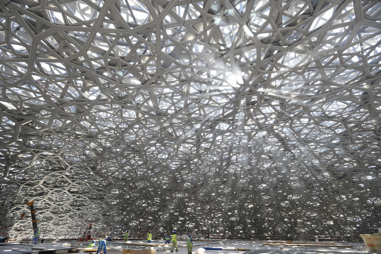 La majestuosa cúpula del Louvre Abu Dhabi filtra la luz solar creando un efecto de “lluvia de luz”. Interior de la cúpula del Louvre Abu Dhabi mostrando patrones de estrellas y luz natural tamizada.