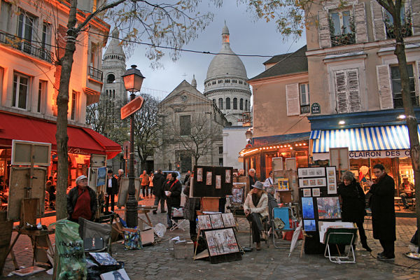 Vista de Place du Tertre en Montmartre, París, con artistas pintando al aire libre y terrazas de cafés típicos.