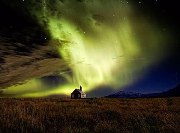 Aurora boreal en los cielos de Islandia Aurora boreal iluminando el cielo nocturno sobre una pequeña cabaña en Islandia.