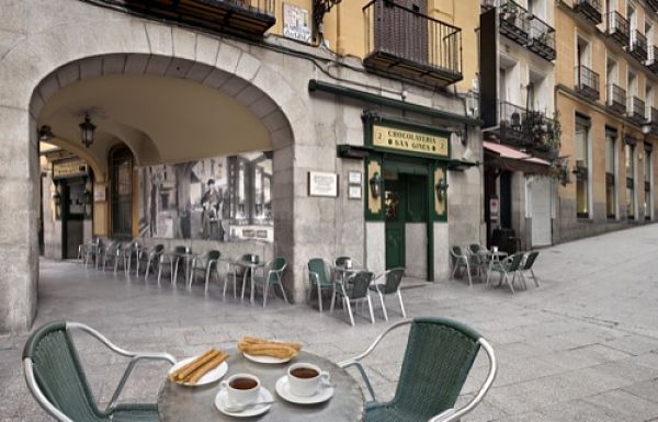 Cafés y bares tradicionales de Madrid Terraza de un café tradicional en una calle de Madrid, con churros y café sobre una mesa.