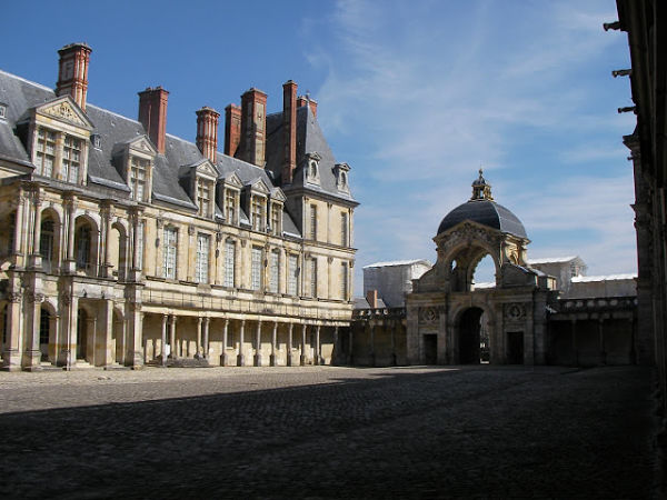 Palacio de Fontainebleau: historia, arte y arquitectura real francesa. Fachada principal del Palacio de Fontainebleau en Francia, con jardines simétricos, cielo despejado y arquitectura renacentista.