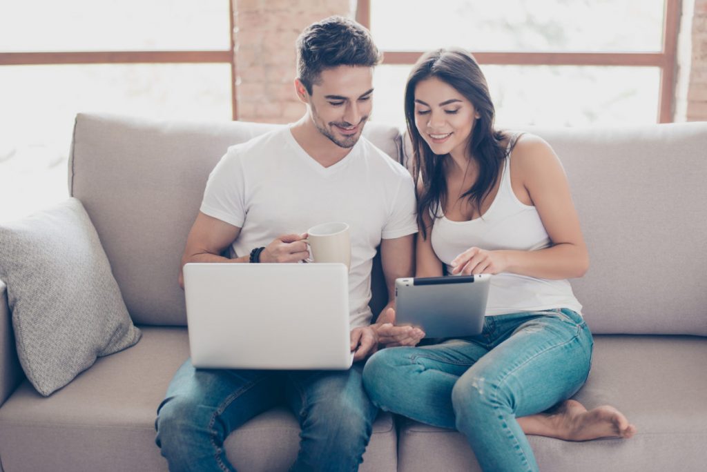 Pareja planificando un viaje en línea con laptop y tablet en casa