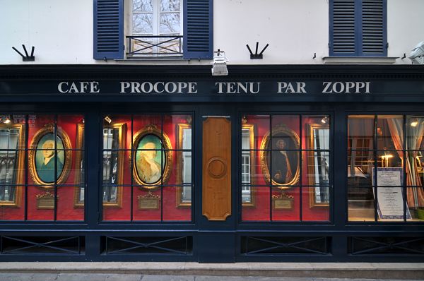 esta el nombre sobre chapa negra vidriera de cafe le procope, se ven atras cuadros con imagenes sobre pared roja