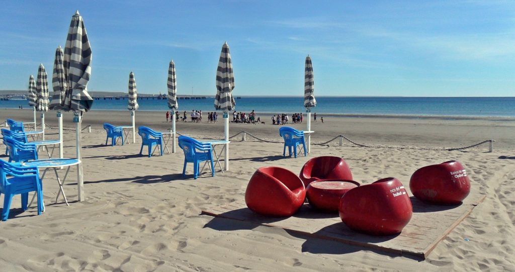 Playa céntrica de Puerto Madryn en verano laya de Puerto Madryn con sombrillas, sillas y turistas disfrutando del verano frente al mar calmo del Golfo Nuevo, Patagonia argentina.