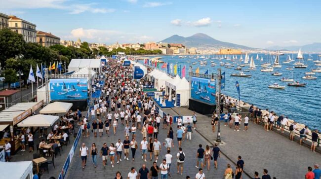 Cómo vivir la America’s Cup 2027 desde la costa de Nápoles Público junto al paseo marítimo de Nápoles durante un evento náutico con veleros y el Vesubio al fondo