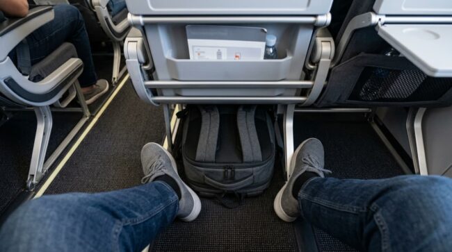 Mochila colocada debajo del asiento delantero de un avión como artículo personal
